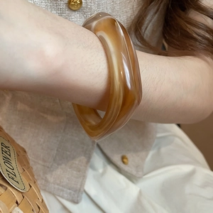 Detail of amber acrylic resin bangle with marble texture on an earthy knit background