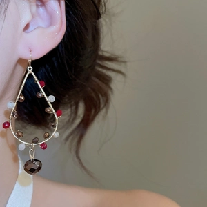 Close-up of model wearing beaded crystal hoop earrings with ethnic tassel pendants