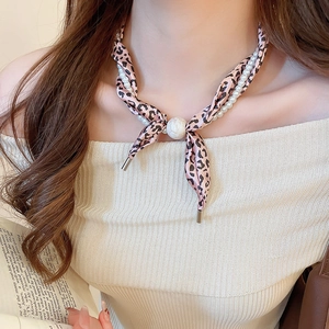 Détail du ruban léopard rose et du collier double épaisseur en perles blanches