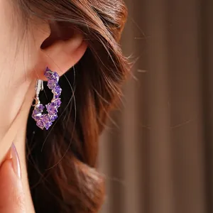 Elegant C-shaped earrings with purple faceted crystals and silver-tone claw setting on model