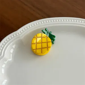 Macro view of a cute yellow pineapple hair claw clip with green leaves on ceramic plate