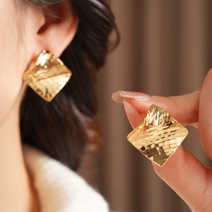 Détail macro de boucles d'oreilles carrées dorées texturées portées à l'oreille et à la main