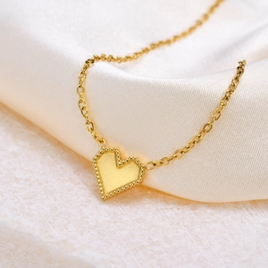 Macro detail of gold heart necklace with beaded border on elegant white silk background