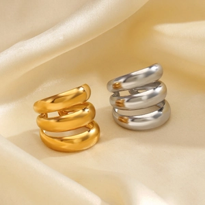 Anelli ondulati a tre strati in oro e argento su sfondo di seta color beige