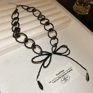 Detail view of a black beaded bow necklace with grey crystal accents on a velvet display