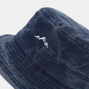 Macro detail of mountain peak embroidery and washed cotton texture on navy bucket hat