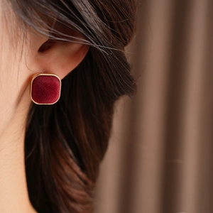 Close-up of a burgundy velvet square stud earring with a gold metal edge on a model