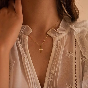 Close-up of minimalist gold cross necklace worn by a model on a lace outfit