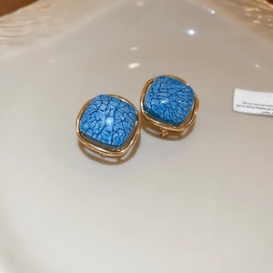 Détail de boucles d'oreilles carrées bleues avec cadre doré et texture en émail