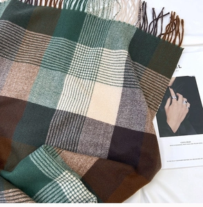 Detailed close-up of thick plaid cashmere scarf with soft fringes and green-brown check
