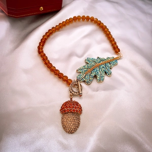 Macro detail of acorn and leaf pendants on beaded necklace with vintage gold OT toggle clasp