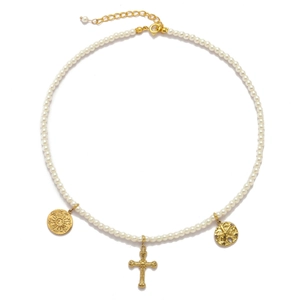 Detail of pearl necklace featuring golden cross and sun emblem charms on white surface
