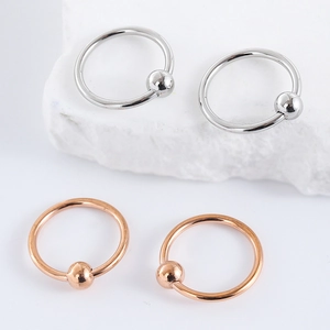 Minimalist stainless steel nose and lip rings in silver and rose gold on white stone