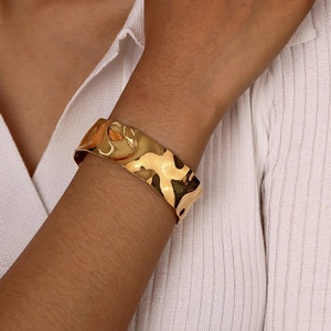Detail of wide gold C-shaped cuff bracelet with irregular wave texture on wrist