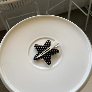 Detail of a star-shaped black hair clip with white polka dots on a minimalist stand