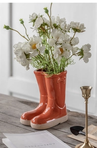 Creative orange ceramic rain boot vase with white daisies on a rustic wooden table