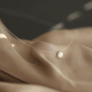 Macro shot of natural pearl pendant on invisible line over champagne silk background
