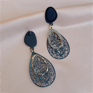 Detailed view of black and gold drop earrings with intricate laser-cut floral patterns