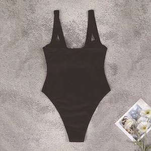Flat lay of a black one-piece swimsuit with wide straps and high-cut leg on a textured background