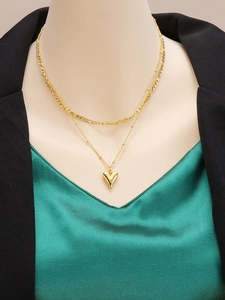 Dettaglio della collana a doppio strato dorata con maglia Figaro e ciondolo a cuore