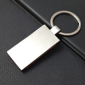 Close-up of a blank rectangular silver metal keychain on a black textured leather surface