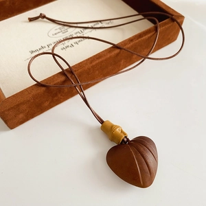 Macro shot of dark brown heart-shaped wood pendant on a brown suede jewelry tray