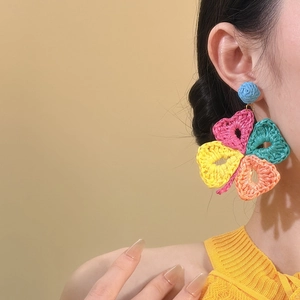 Orecchini a fiore in rafia intrecciata colorata per donna indossati da una modella in estate