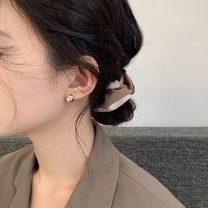 Close-up of minimalist silver bean stud earring worn by a model in a brown blazer