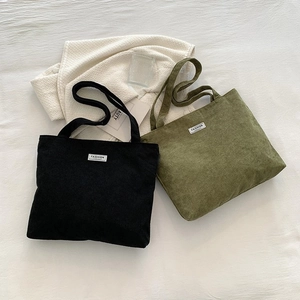 Flat lay of large corduroy tote bags in black and olive green on a textured white bed