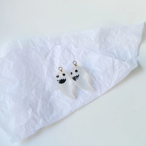 Macro shot of cute ghostly resin charms with gold hangers on white textured paper