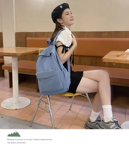 Blue canvas backpack shown on a model in a cafe setting, featuring a minimalist aesthetic