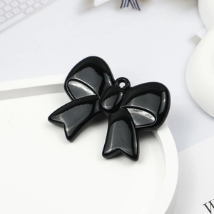 Macro shot of a glossy black bow-knot charm with hanging hole on a white tray