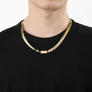 Detail of a gold flat Cuban link chain necklace with a rectangular engraved nameplate charm