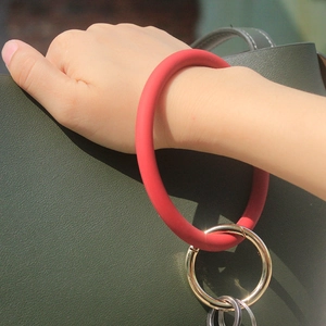 Red silicone O-ring bracelet keychain with gold metal clasp worn on wrist with bag