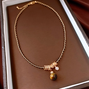 Detail of tiger eye stone and gold ring pendant on minimalist chain with beads