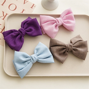 Flat lay of four linen bow hair clips in purple, pink, blue, and brown on a tray
