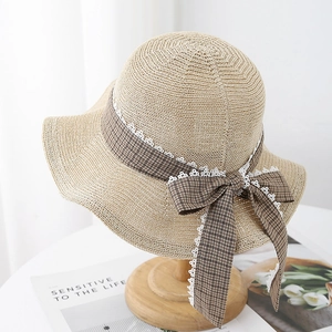 Detail of beige straw sun hat featuring brown plaid ribbon and white lace trim bow