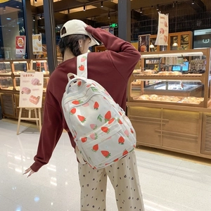 Detail of the white canvas backpack featuring red strawberry prints and zipper pocket