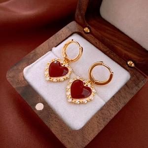 Detail of gold-plated heart earrings with red zircon in a luxury wooden jewelry box