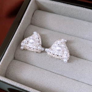 Macro view of triangle stud earrings with pearls and zircon in a grey jewelry box