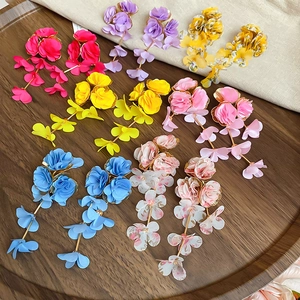 Flat lay of colorful chiffon flower tassel earrings on a wooden tray with linen fabric