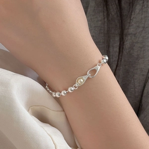 Detailed shot of a silver beaded bracelet with teardrop pearl charm on a model's wrist