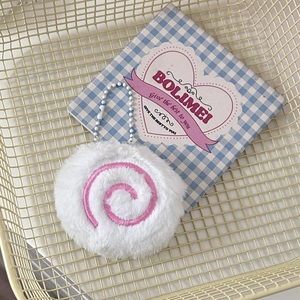 Close-up of a cute fish cake plush keychain with pink spiral on a grid background