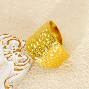 Macro detail of gold hammered texture wide band ring on a decorative marble surface