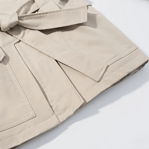 Close-up of beige trench coat with stand collar, waist tie bow, and premium stitching