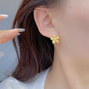 Detailed close-up of golden six-petal flower stud earring on a model's earlobe