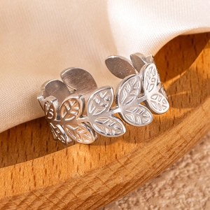 Macro shot of silver stainless steel leaf ring on a wooden tray with satin backdrop