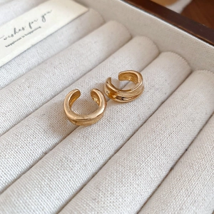Detailed close-up of gold geometric C-shape ear cuffs on a soft white velvet background