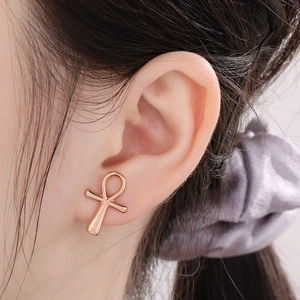 Close-up of polished rose gold Ankh cross stud earrings worn on ear for detail