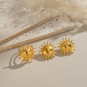 Golden sun-shaped stainless steel earrings on a beige stone and dried reed display